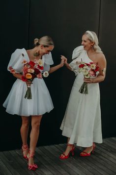 two women in white dresses standing next to each other with bouquets on their hands