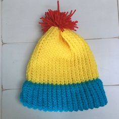 a yellow and blue knitted beanie with a red pom - pom