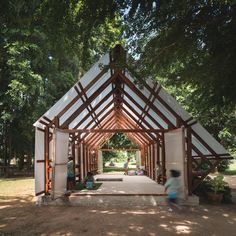 a wooden structure with white walls and wood beams in the middle of a park area