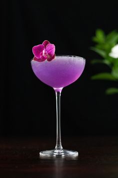 a purple drink with a pink flower on the rim in front of a black background