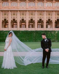 a bride and groom standing in front of a building with a veil blowing in the wind