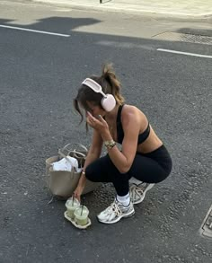 a woman squatting on the ground with headphones in her ears and looking down