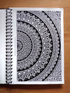 an open spiral notebook with black and white designs on the cover, sitting on top of a wooden table