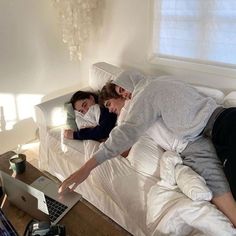 two people laying on a bed and one is using a laptop while the other looks at something