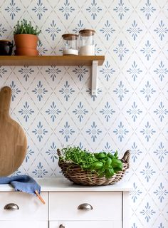 a wooden cutting board sitting on top of a white dresser next to a basket filled with greens