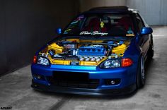 a blue car parked in a garage with its hood up and the engine bay open