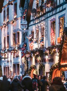 many people are walking down the street in front of buildings decorated with christmas lights and garlands