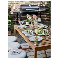 a wooden table topped with lots of plates of food next to a bbq grill