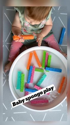 a baby sitting in front of a white bowl filled with colorful foam blocks that spell out the word baby sponge play