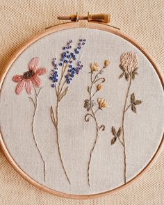 embroidery with flowers on it is displayed in a wooden hoop, along with other stitches and threads