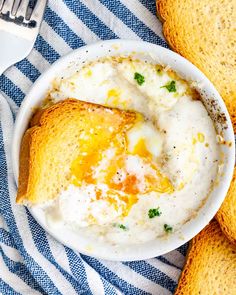 a white bowl filled with food on top of a blue and white table cloth next to bread