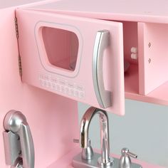 a pink toy microwave oven sitting on top of a counter next to a faucet