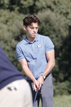 a young man holding a golf club in his right hand and looking down at the ground