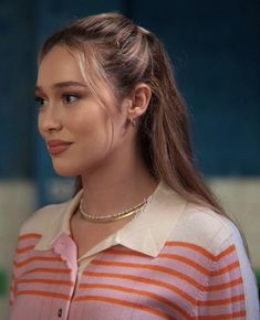 a woman with long hair wearing an orange and white striped shirt is looking off to the side