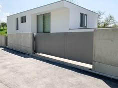 a white house sitting on the side of a road next to a cement wall and fence