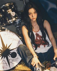 a woman sitting on the floor next to a drum set