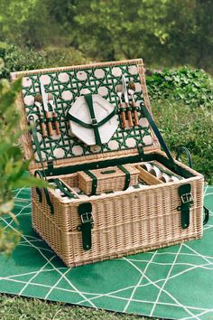 a wicker picnic basket with utensils in it on a green tablecloth