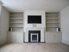 an empty living room with built in bookshelves and a flat screen tv above the fireplace