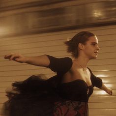 a woman in a black dress riding a skateboard on the street with her arms outstretched