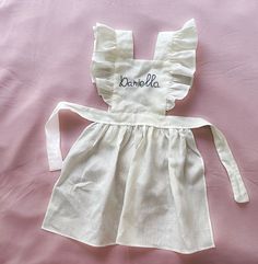 a white dress with ruffles and the word bombla on it is laying on a pink sheet