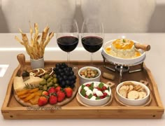 a wooden tray topped with different types of food and wine glasses filled with red wine