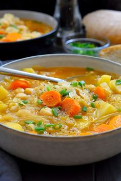 two bowls of soup with carrots, potatoes and bread on the table next to each other