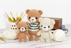 three crocheted teddy bears sitting next to each other in front of yarn balls