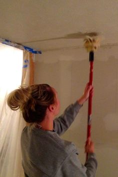 a woman is painting the ceiling in her home