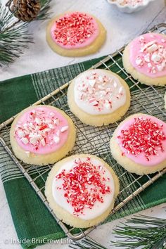 cookies decorated with pink and white icing on a cooling rack next to pine cones