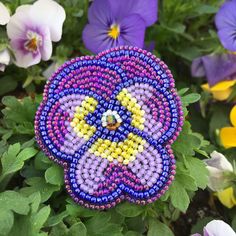 a colorful beaded flower surrounded by purple and yellow flowers