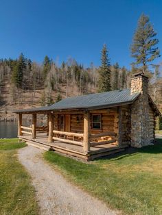 a log cabin sits in the middle of a grassy area next to a body of water