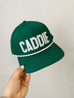 a person holding up a green cap with the word caddie written on it in white