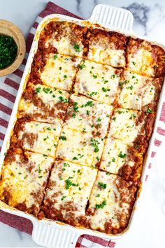 lasagna casserole with meat and cheese in a white dish on a red and white checkered towel