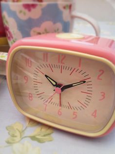 a pink alarm clock sitting on top of a table next to cups and saucers