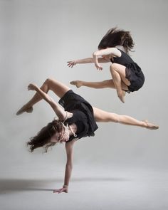 two young women in black dresses are dancing on their feet and arms, with one holding the other's leg