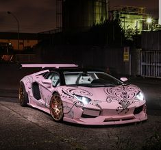 a pink sports car parked in front of an industrial building at night with lights on