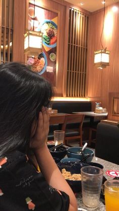 a woman sitting at a table with food and drinks in front of her on the phone