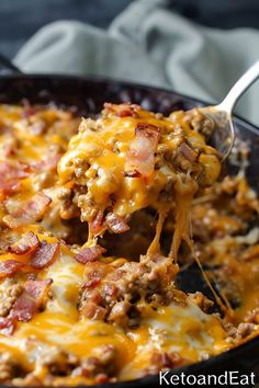 a spoon full of cheesy ground beef casserole being lifted from a skillet