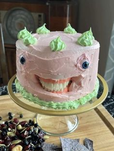 a pink cake with green frosting and smiling face on a gold platter next to crackers