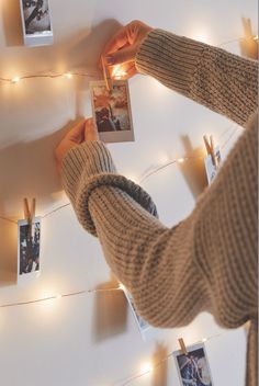 a person holding up pictures on a string with lights strung around the wall behind them