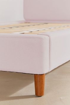 a pink bed frame with wooden legs and no sheets on the bottom, in front of a white wall