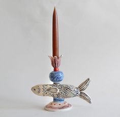 a candle holder with two fish on it and a red candle sticking out of the top