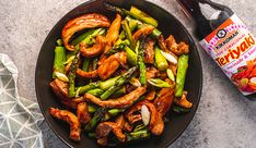 stir fry with chicken and asparagus in a bowl next to a bottle of hot sauce