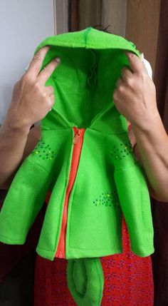 a person is holding up a green jacket with an orange zipper and red dress underneath it