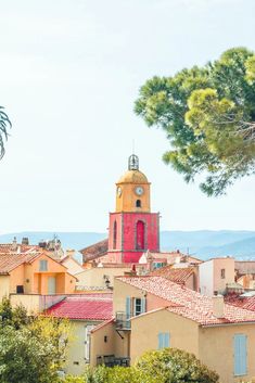 a red and yellow clock tower in the middle of buildings with trees on both sides