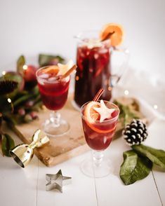 two glasses filled with red liquid and garnished with orange slices on a cutting board