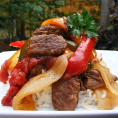 a white plate topped with meat and veggies on top of rice covered in sauce