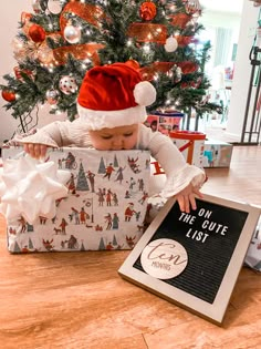 a small child in a santa hat opening a christmas gift under a tree with presents