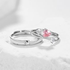 two silver rings with pink and white stones on them sitting on a marble table top