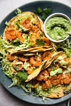 a plate filled with shrimp tacos and guacamole sauce on the side